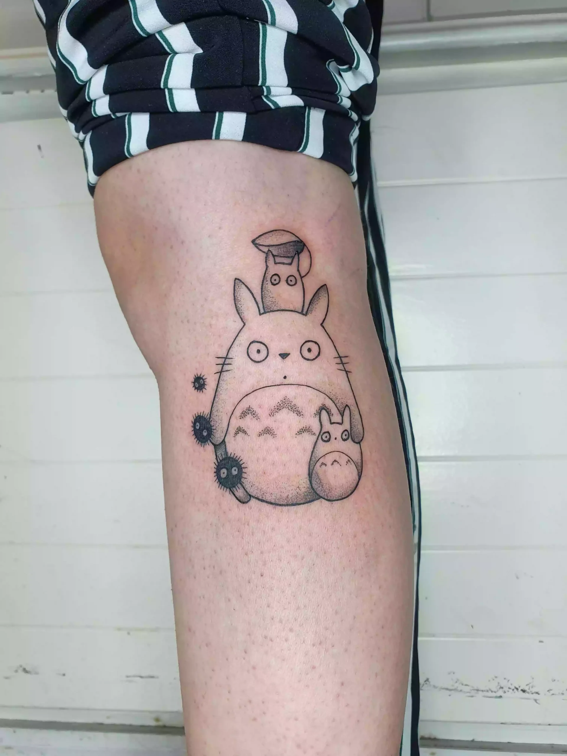 Lineart Tattoo der Totoro-Charaktere mit Russmännchen an der Wade