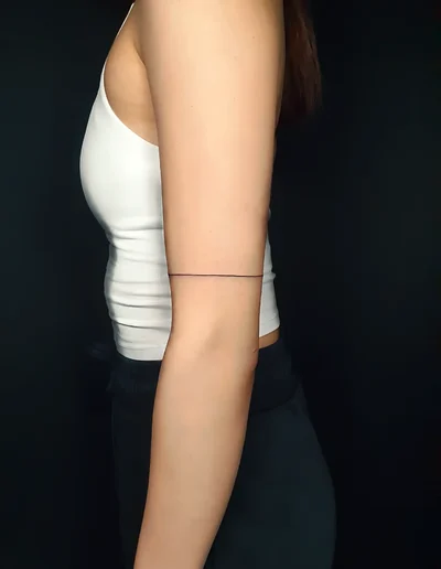Minimalistisches Fineline Armband-Tattoo am Oberarm.