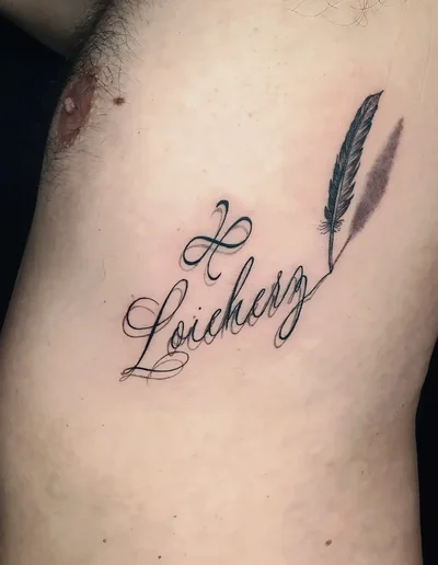 Realistic Tattoo eines kalligrafischen Schriftzugs „Loicherz“ mit Herzsymbol und fein schattierter Feder auf der linken Körperseite.
