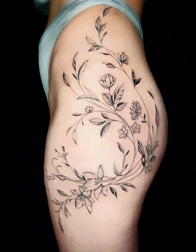 Realistic Tattoo florales Design am Oberschenkel mit filigranen Blumen und Blättern.