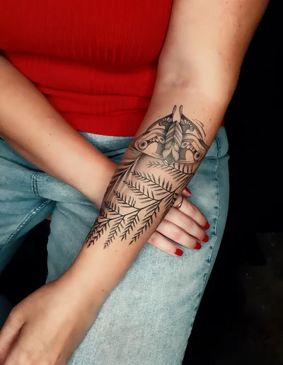 Realistic Tattoo auf dem Unterarm mit detailliert gestochenem Nachtfalter und Farnblättern.