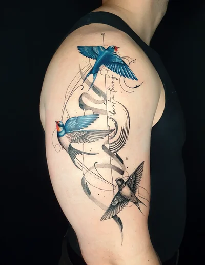Realistic Tattoo von drei Schwalben mit blauen und grauen Akzenten, dynamischen Linien und kalligrafischen Elementen auf dem Oberarm.
