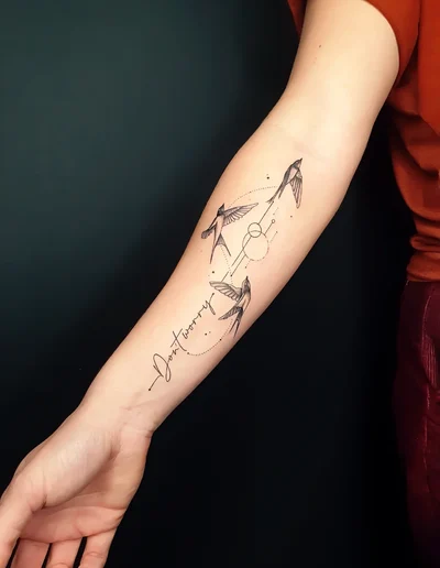 Realistic Tattoo von drei Schwalben mit feinen geometrischen Linien und dem Schriftzug &amp;quot;Don&amp;#039;t worry&amp;quot; auf dem Unterarm.