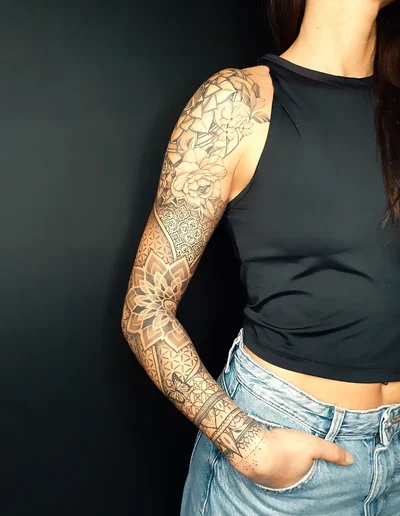 Full-Sleeve-Tattoo mit floralen Elementen, Mandalas und Dotwork-Mustern auf dem Arm einer Frau.
