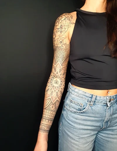 Ganzarmtattoo im Mandala- und Dotwork-Stil mit floralen Motiven und Lotusblume auf dem Unterarm.