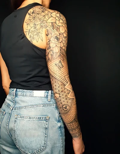 Ganzarmtattoo mit floralen Elementen, Dotwork-Mustern, geometrischen Formen und Schmetterling auf dem Unterarm.