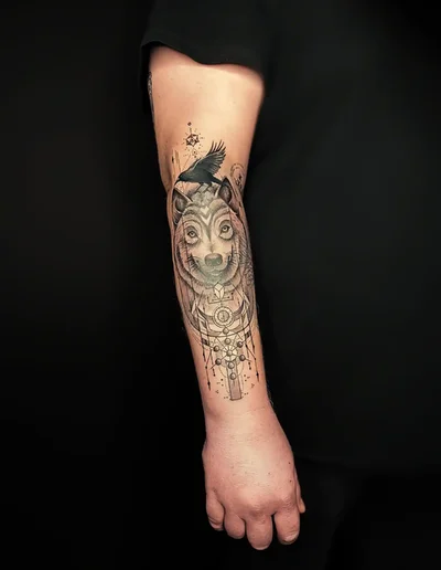 Realistic Tattoo eines Wolfes mit fliegender Krähe und geometrischen Mustern auf dem Unterarm.
