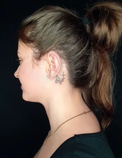 Fineline Schmetterling- und Kreuz-Tattoo hinter dem Ohr.