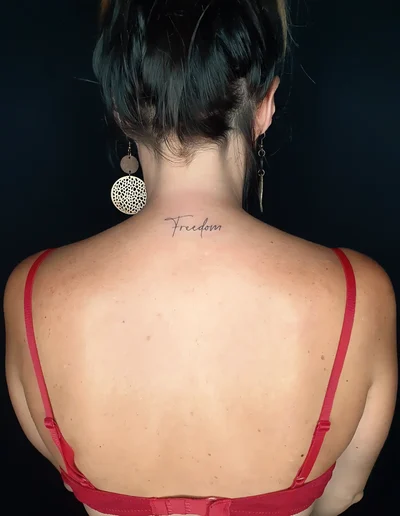 Lettering Tattoo im Fineline-Stil auf dem oberen Rücken mit dem Schriftzug „Freedom“ in feiner, eleganter Handschrift.