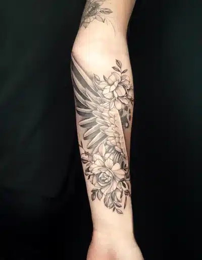 Realistisches Blumen Tattoo mit Engelsflügel am Unterarm, gestochen bei EB Tattoo in St. Gallen – florale Elemente in Black &amp;amp; Grey
