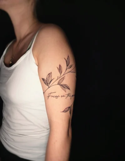 Fineline Blätter Tattoo mit Script „Focus on the good“ am Oberarm bei EB-Tattoo St. Gallen