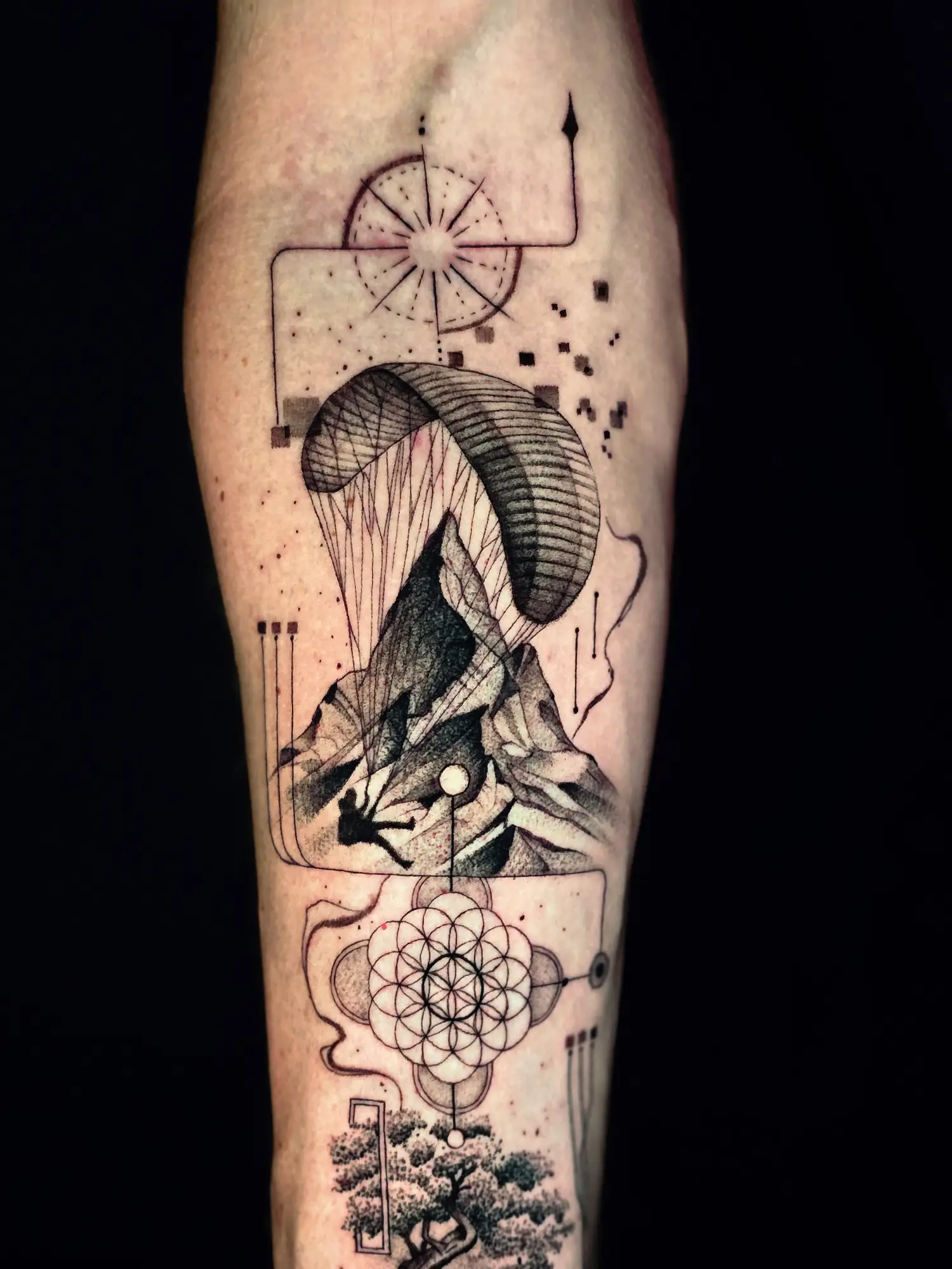 Berglandschaft mit Gleitschirm, Kompass und Flower of Life als Storytelling Tattoo am Unterarm