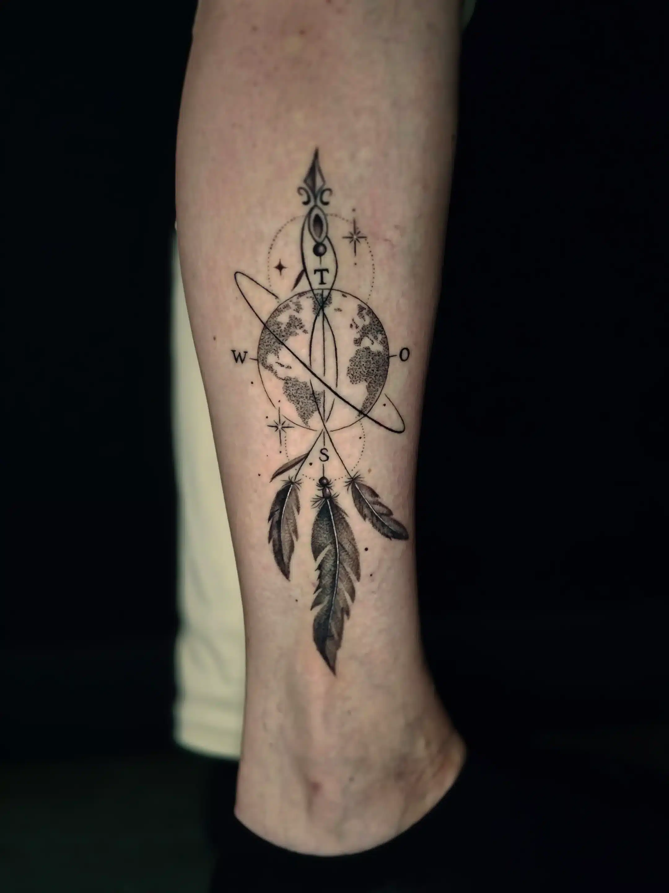 Storytelling Tattoo mit Kompass, Weltkarte und Federn am Unterschenkel, gestochen bei EB Tattoo in St. Gallen