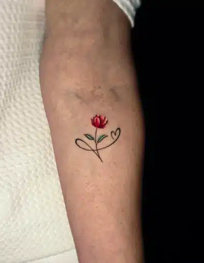 Minimalistisches Blumen Tattoo mit feinen Linien und roter Blüte am Arm, gestochen bei EB-Tattoo St. Gallen
