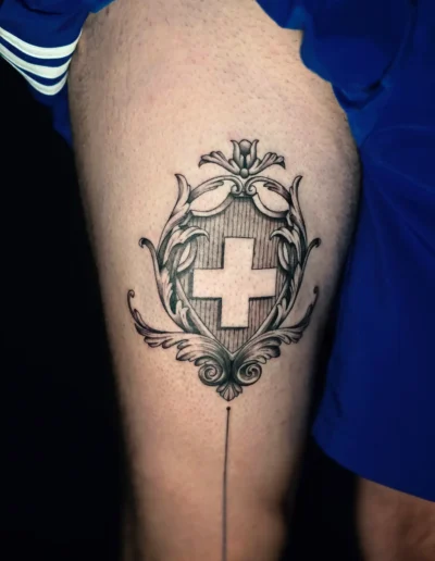 Schweizer Kreuz Tattoo mit ornamentalen Linien und feiner Schattierung am Oberschenkel, gestochen bei EB-Tattoo St. Gallen
