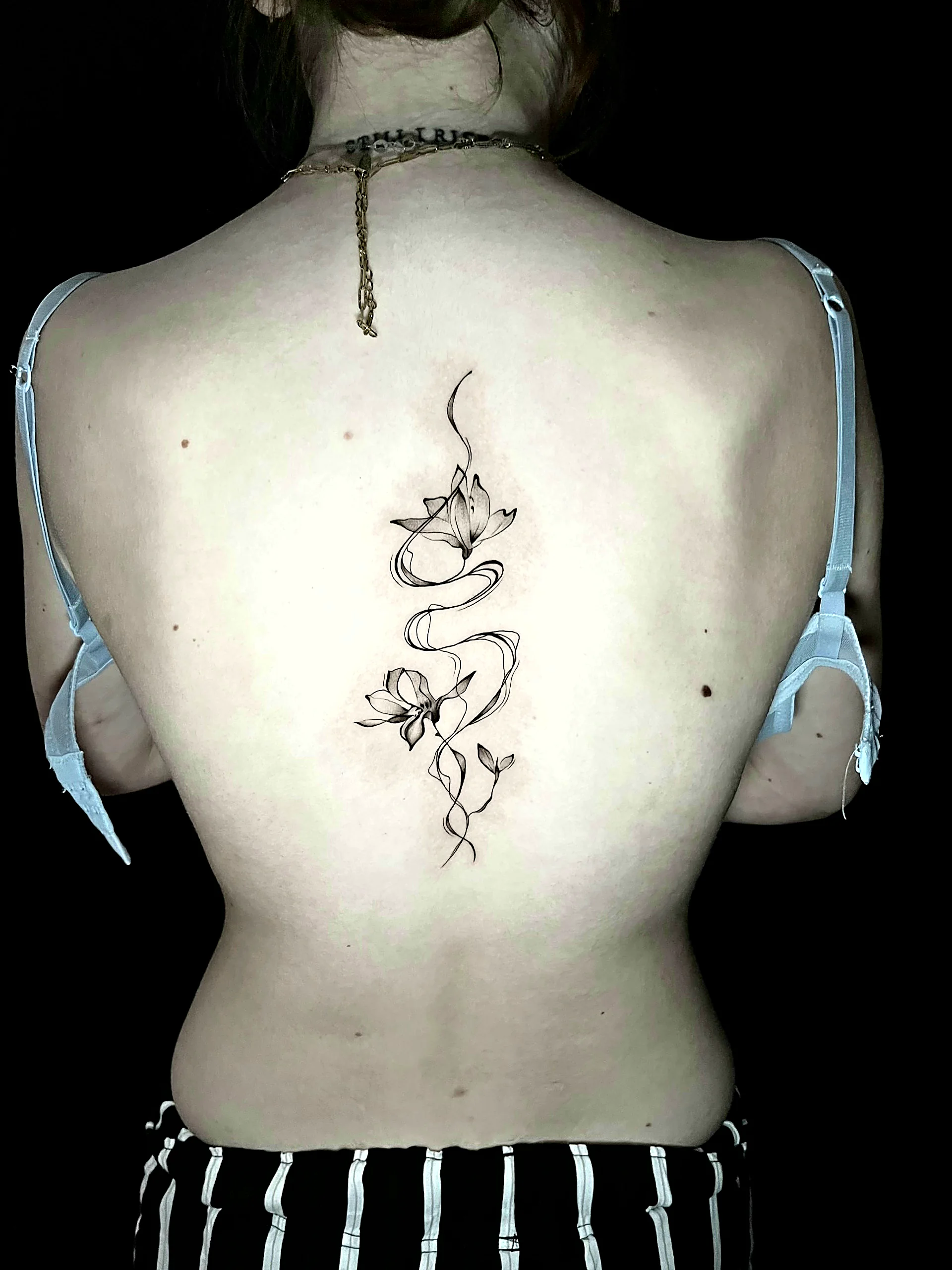 Fineline Blumen Tattoo mit fliessenden Bändern entlang der Wirbelsäule, gestochen von Silas bei EB Tattoo St. Gallen