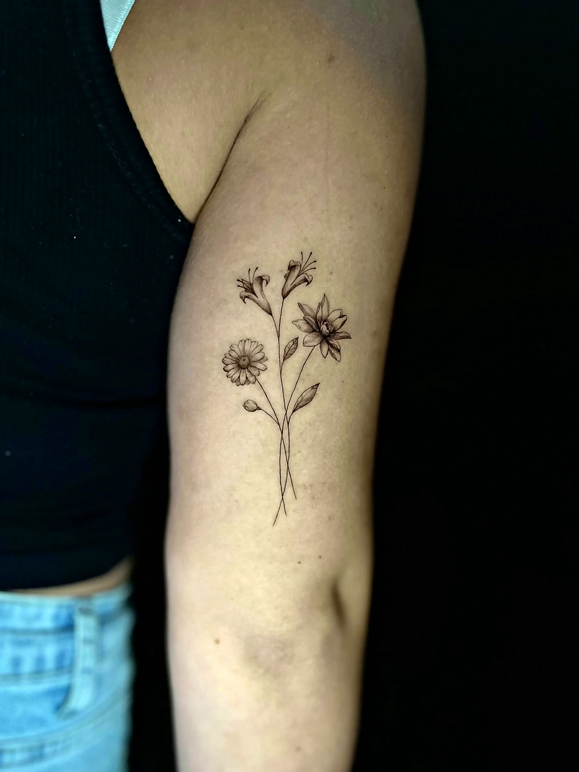 Fineline Wildblumenstrauss Tattoo am Oberarm, gestochen von Silas bei EB Tattoo St. Gallen